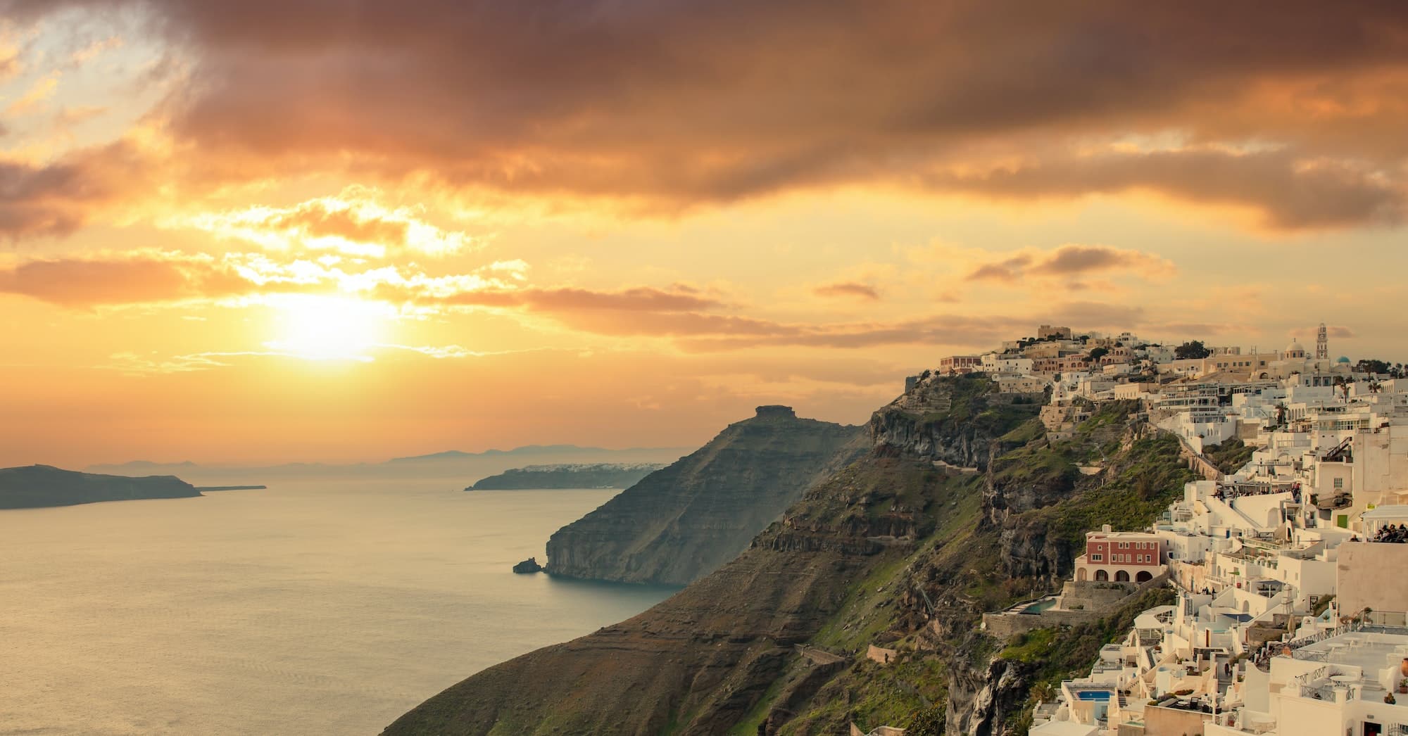 Santorini island, Greece. Fira caldera over Aegean sea, orange color cloudy sky, calm sea