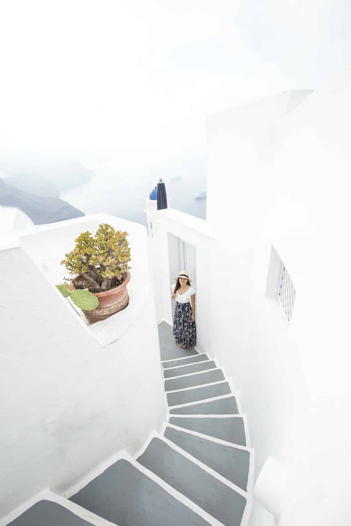 Young woman by a stairway in a patio at a white home while on vacation at santorini Greece