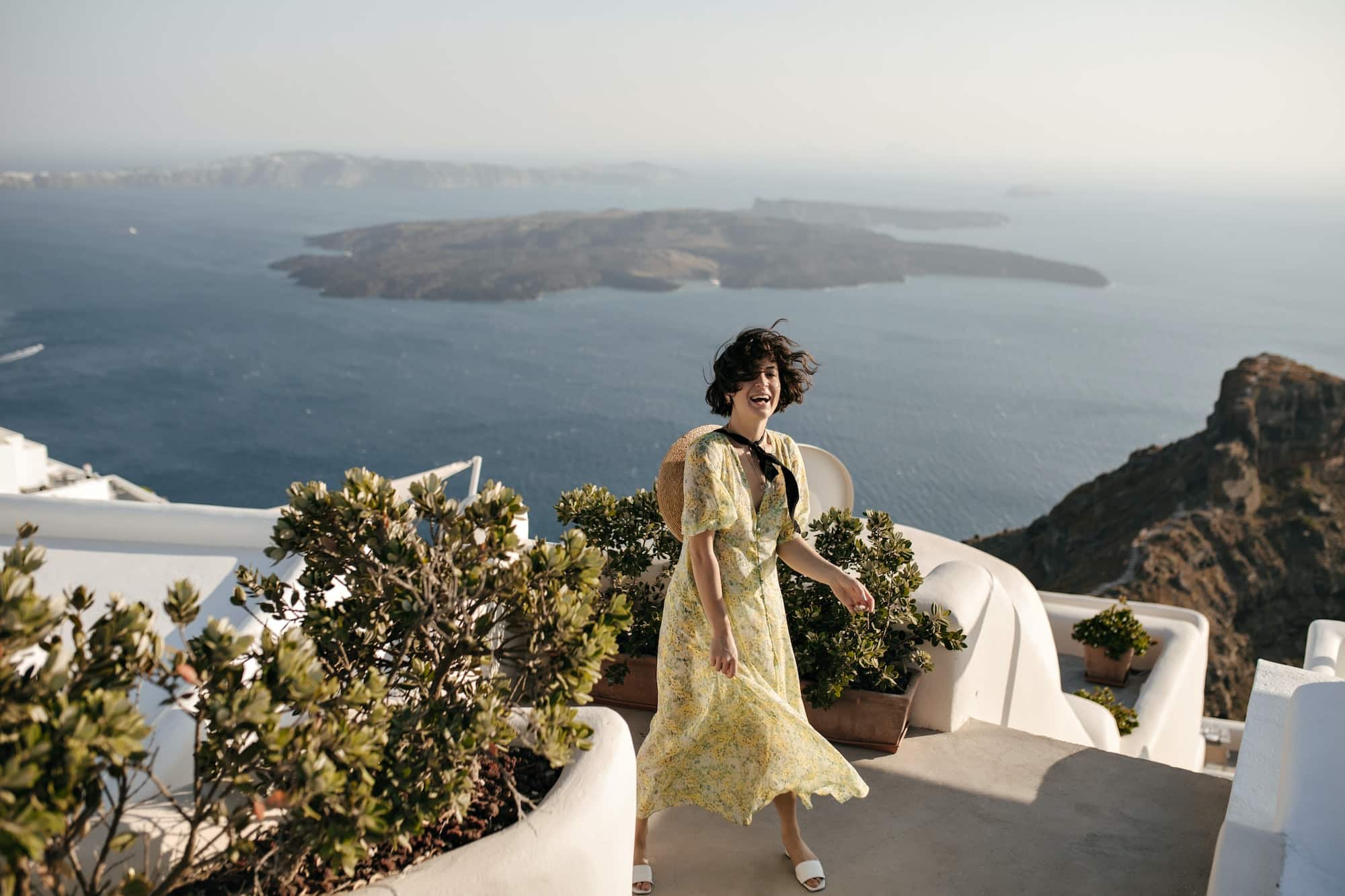 Joyful brunette woman in floral dress smiles sincerely in beautiful place with sea view. Happy char