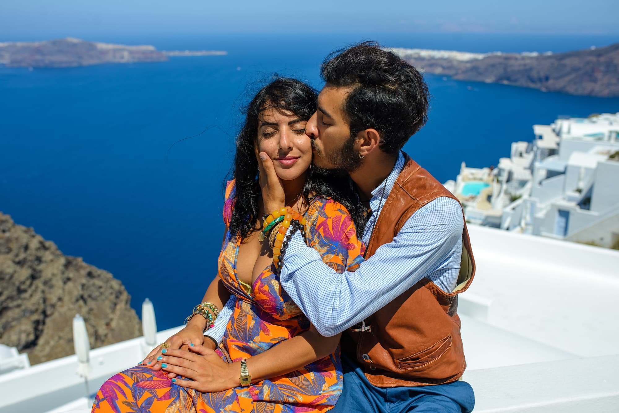 A man and a woman kiss against the backdrop of Skaros Rock on Santorini Island.