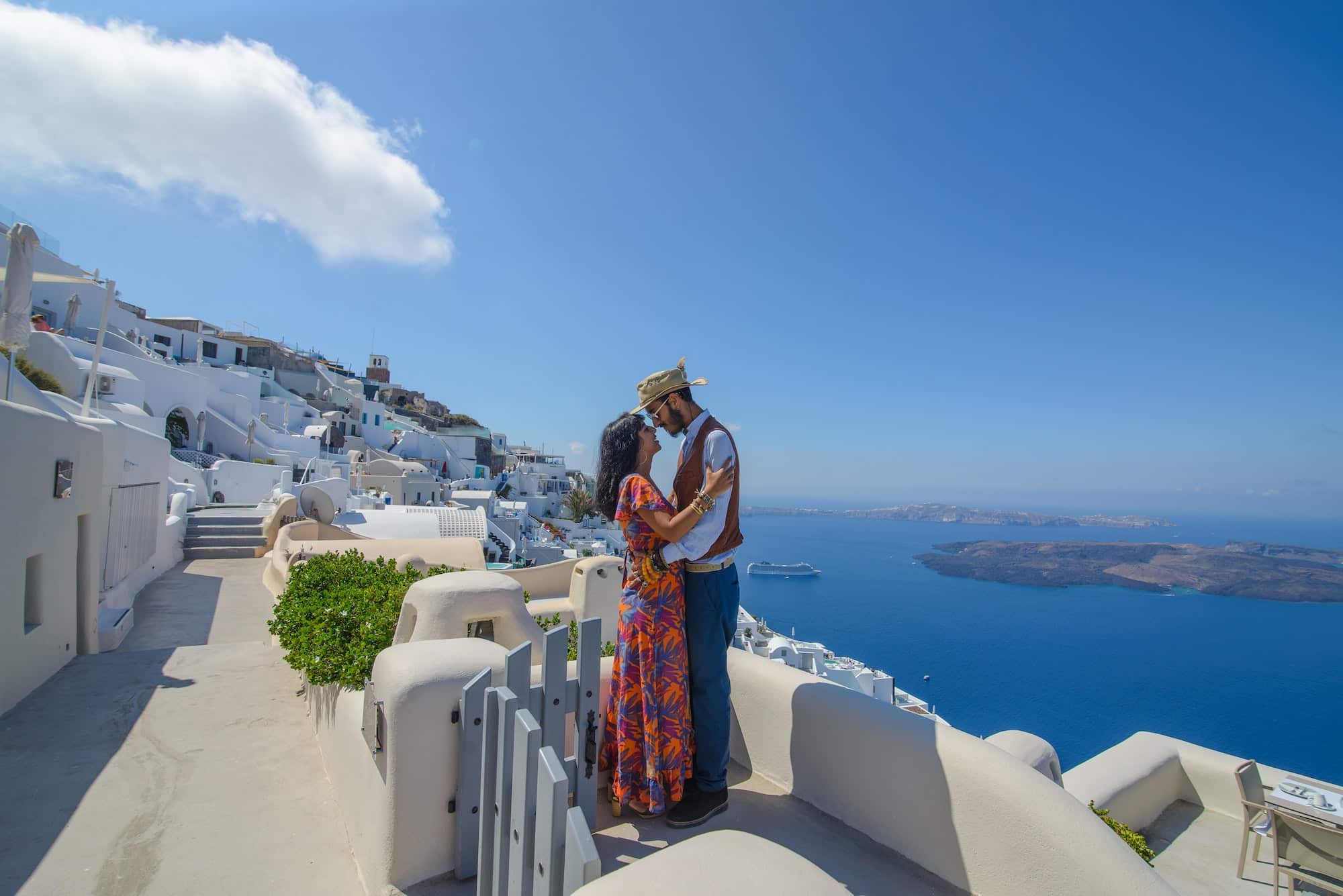 A man and a woman are hugging against the backdrop of Skaros Rock on Santorini Island.