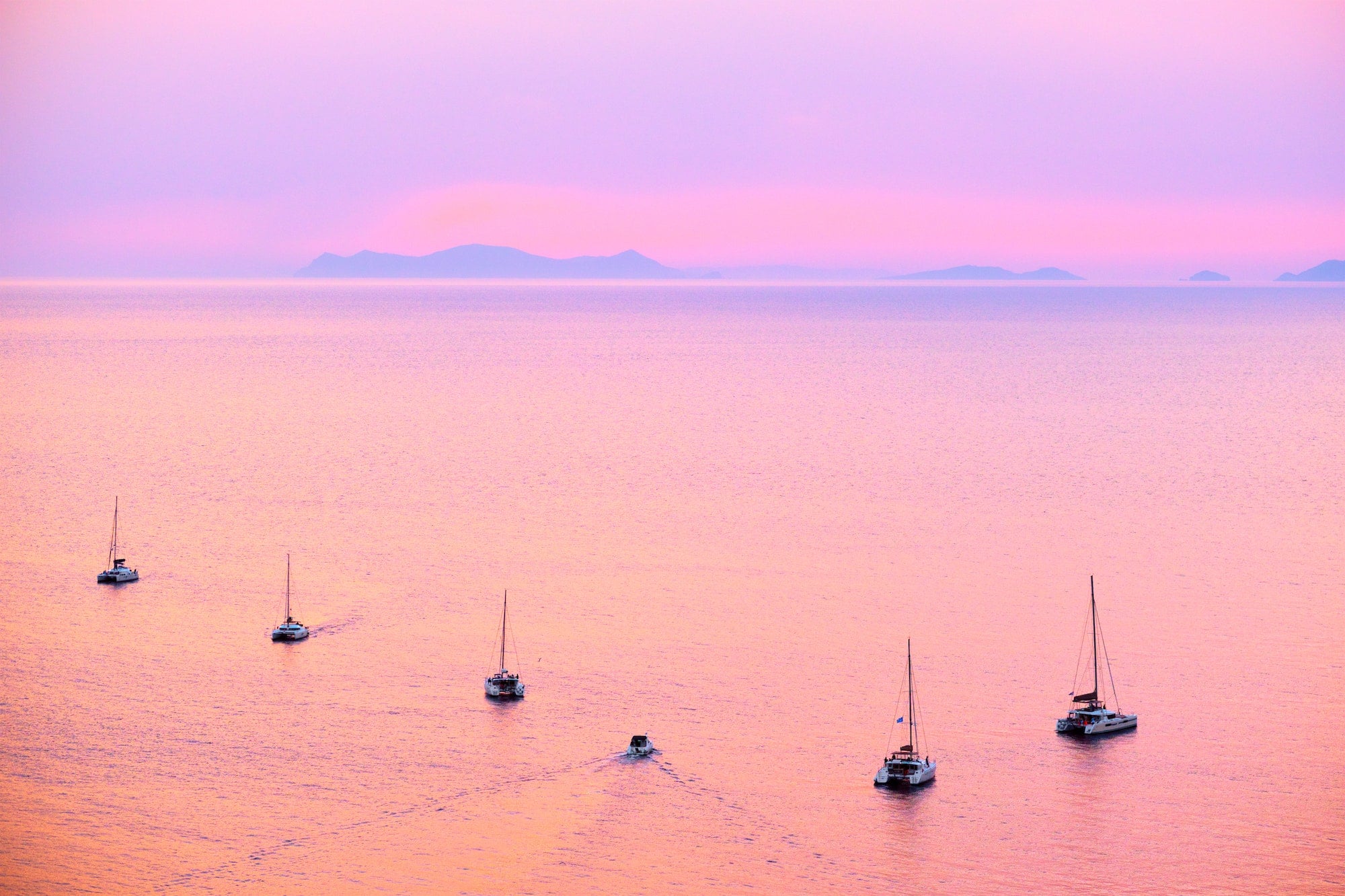 Tourist yachts boat in Aegean sea near Santorini island with tourists watching sunset viewpoint