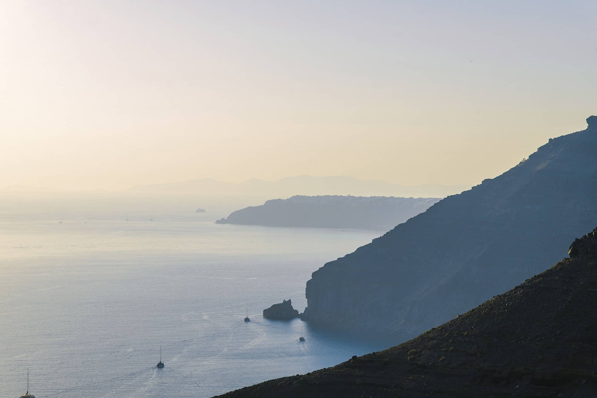 View of the sea and the cliffs from Santorini. Yachts are sailing far.