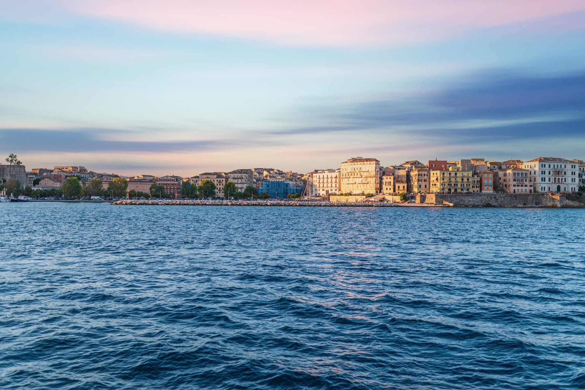 Buildings of Corfu island on shore and sea water at sunset
