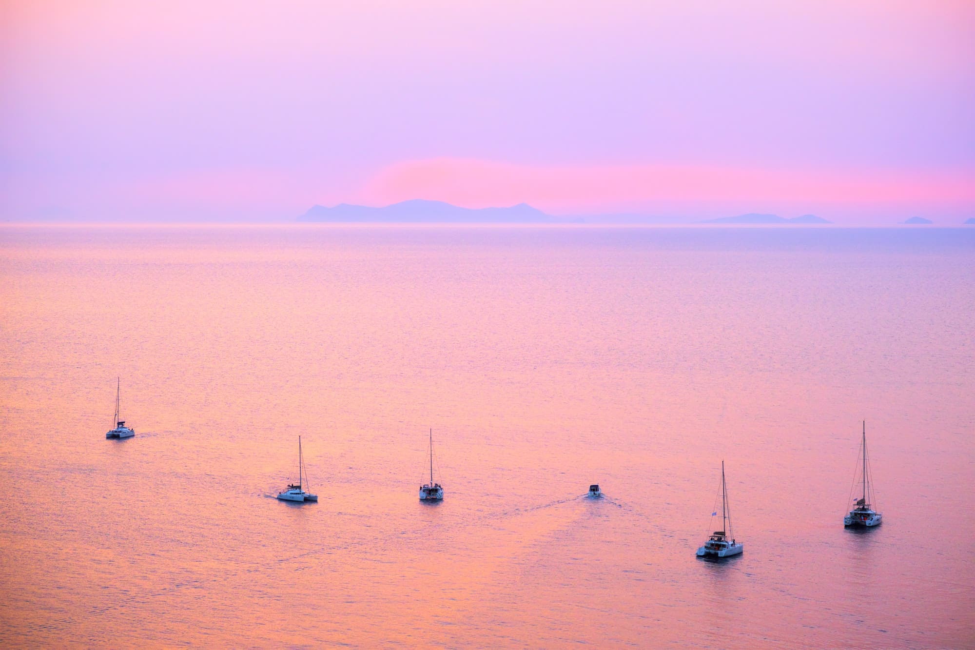 Tourist yachts boat in Aegean sea near Santorini island with tourists watching sunset viewpoint