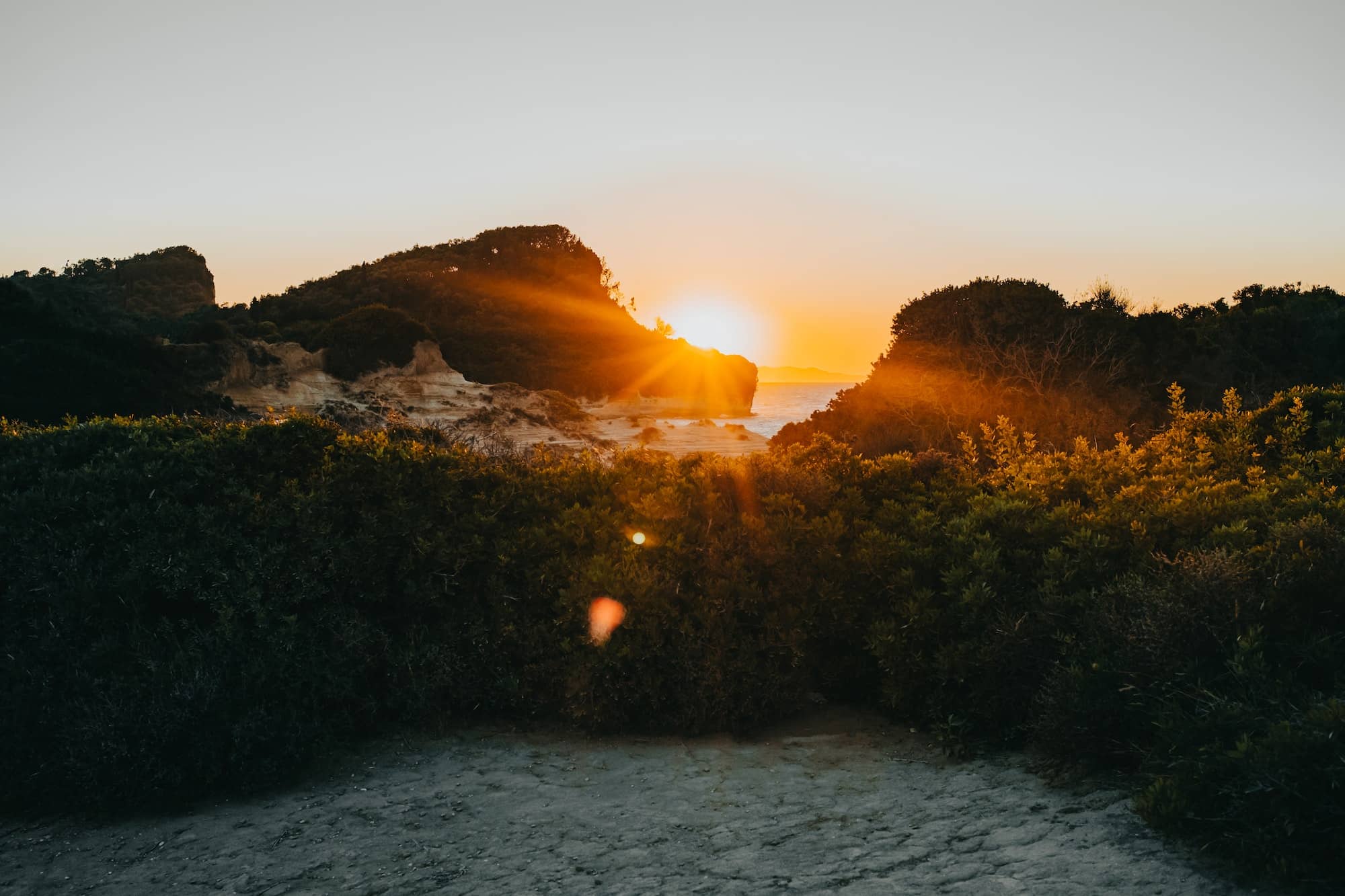 Sun shines through mountain on wild beach. Beautiful sunset background, nature, summer time. Golden