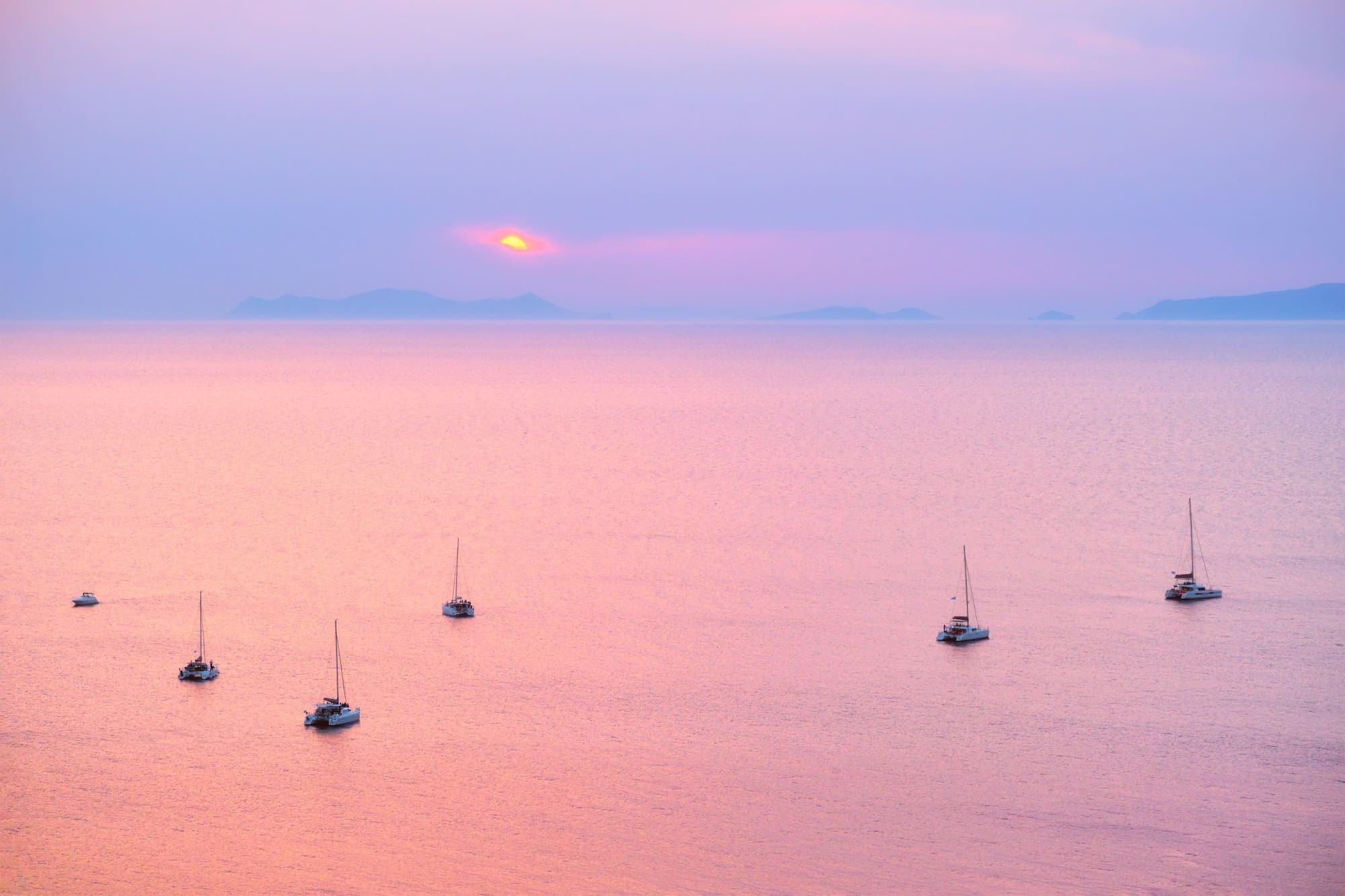 Tourist yachts boat in Aegean sea near Santorini island with tourists watching sunset viewpoint