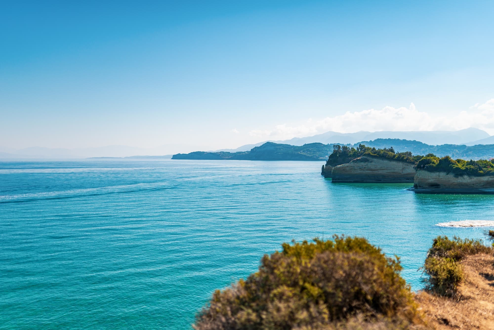 Boats sailing on sea near Corfu island under blue sky