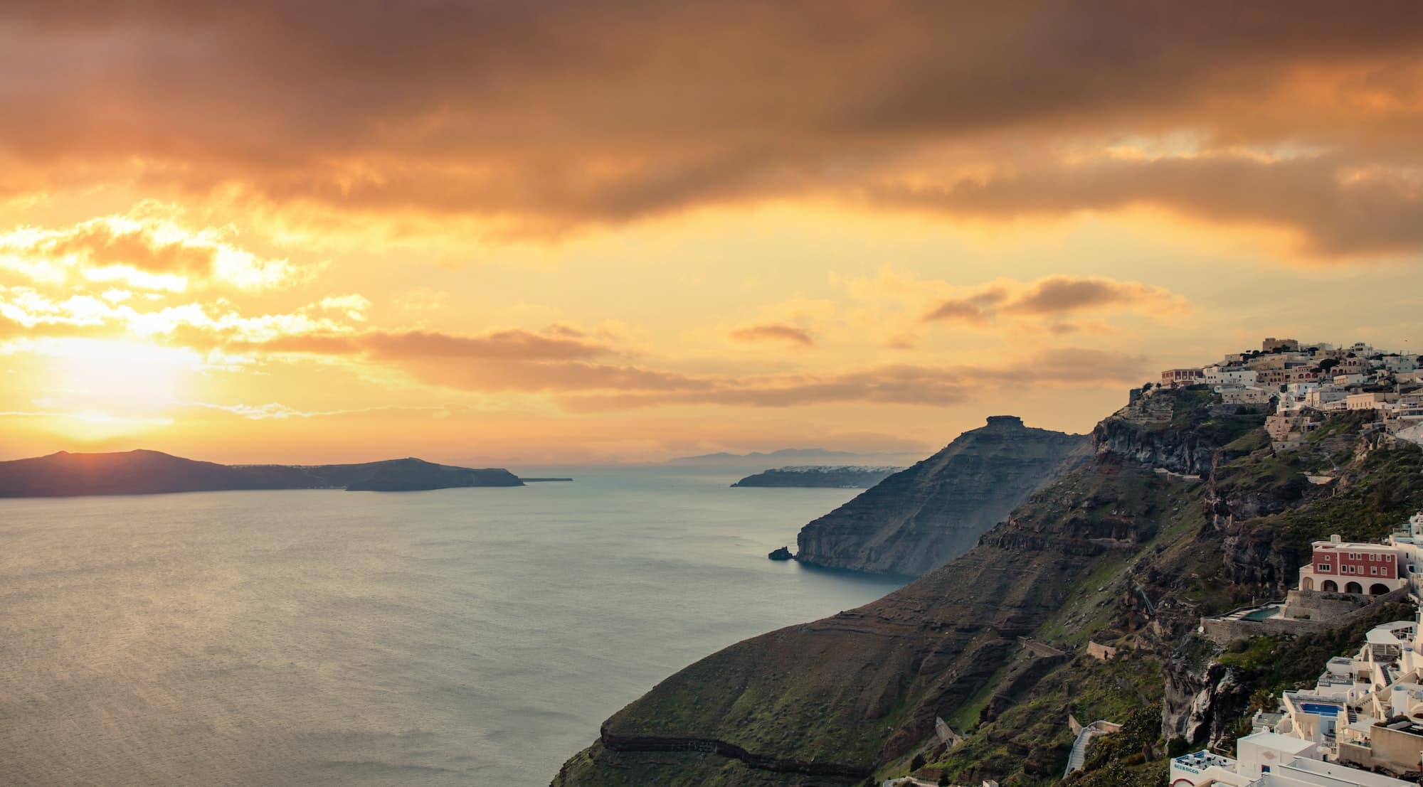 Santorini island, Greece. Fira caldera over Aegean sea, orange color cloudy sky, calm sea