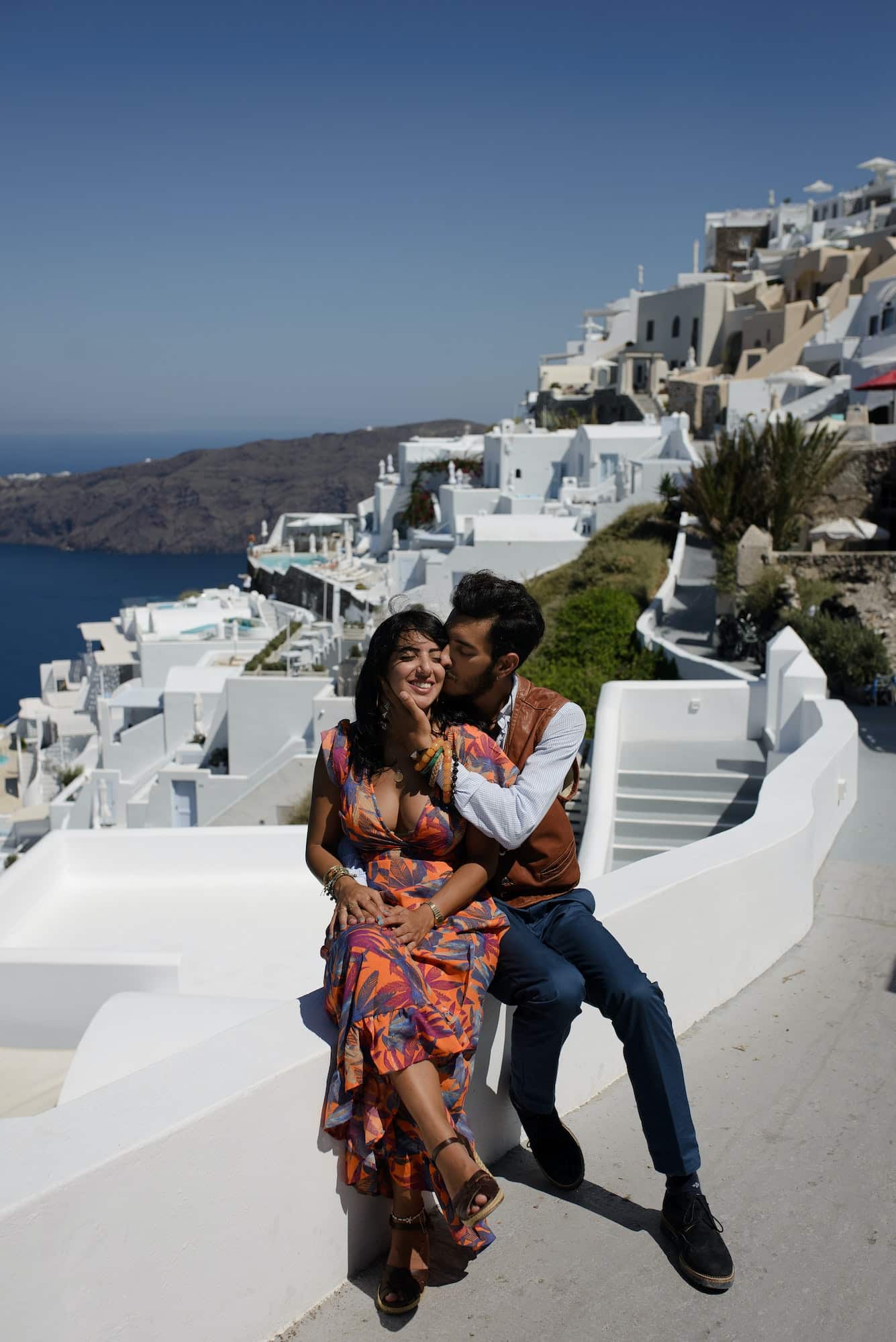 The couple is sitting on the roof in Santorini, hugging and laughing