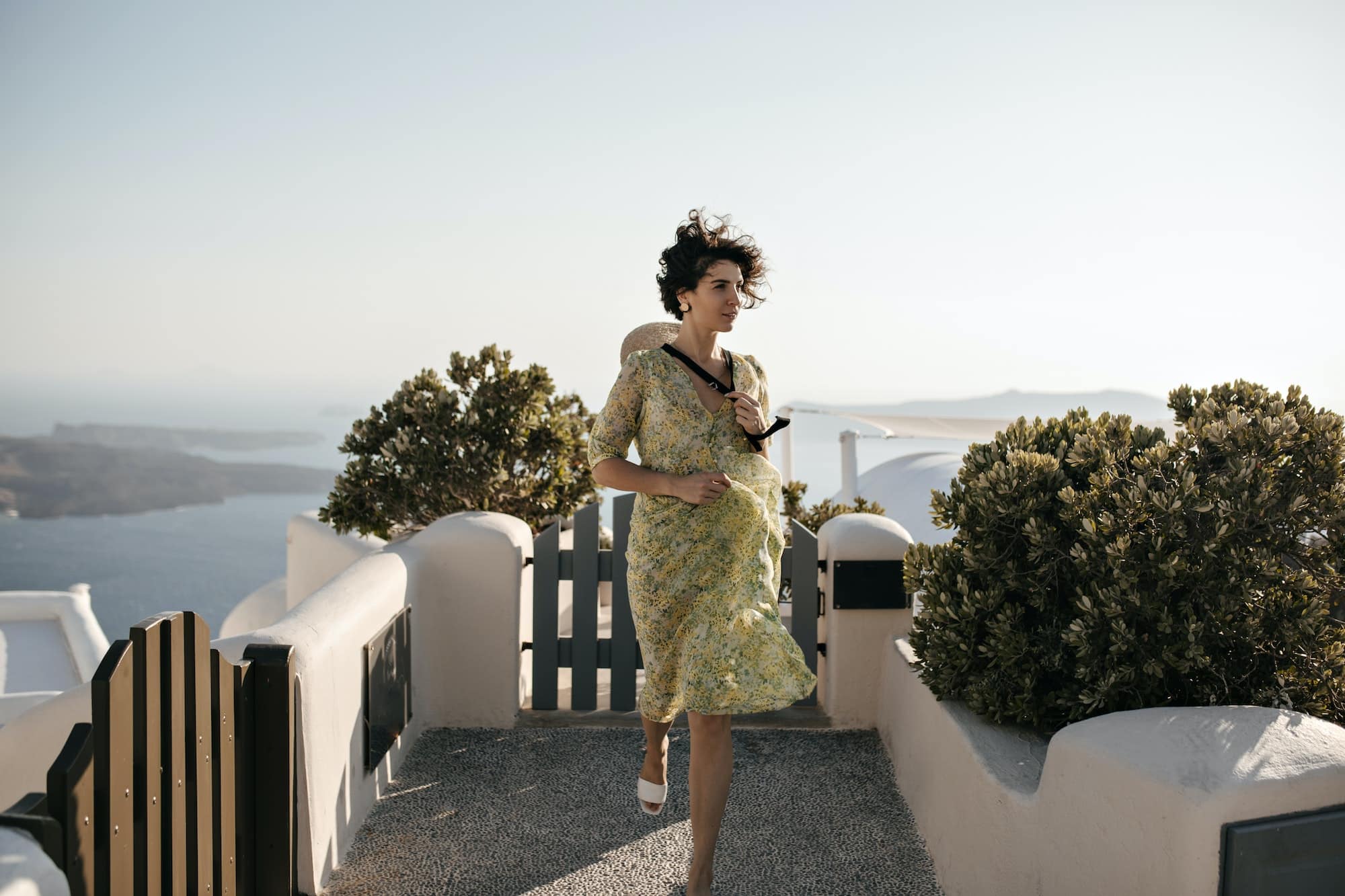 Brunette curly short-haired woman in midi dress runs on sea background. Attractive lady in floral o