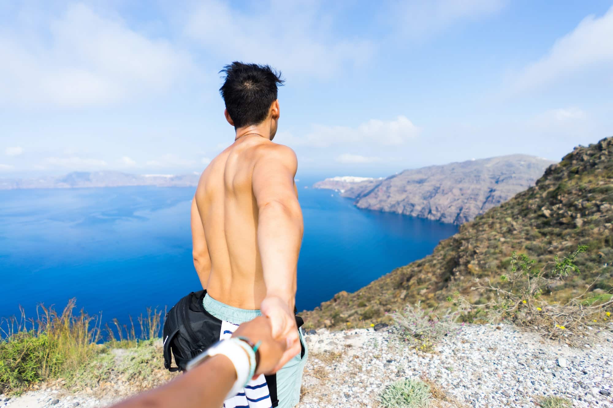 Hiking from Oia to Fira in Santorini, Greece. Holding hands with a view of the ocean and landscape.